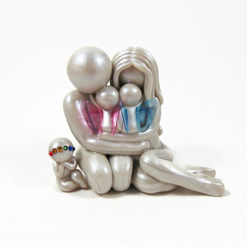 May include: A pearlescent figurine depicting a family of five. The parents embrace two children, with the youngest child seated nearby. The children have pink and blue accents. The youngest child wears a colorful jeweled headband.