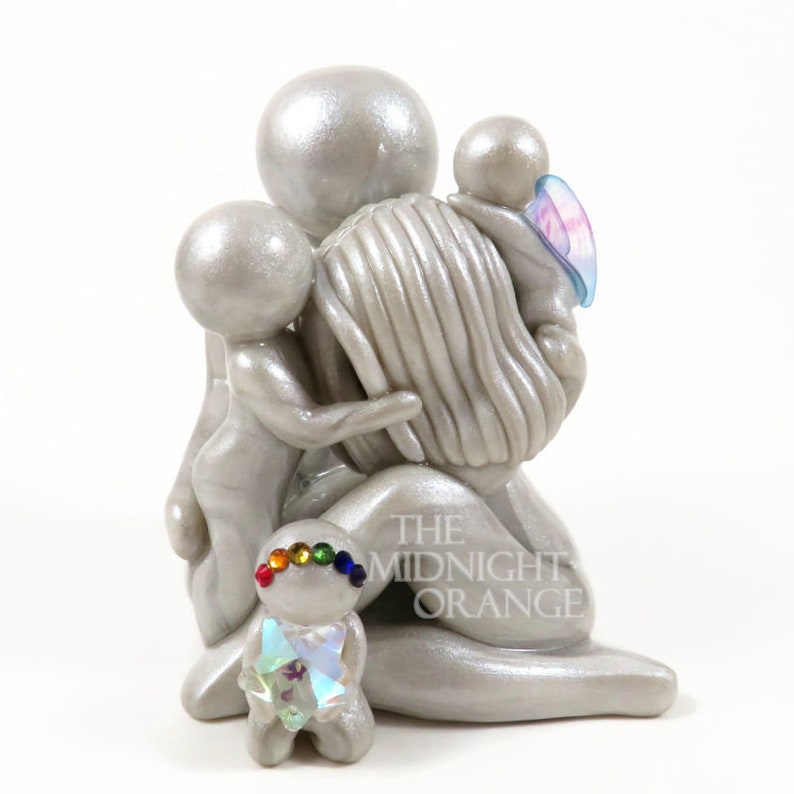 May include: A silver figurine depicting a parent figure embracing three children. One child has a rainbow-colored headband and a crystal-like chest. The figurine has a pearlescent finish. The Midnight Orange is printed on the base.