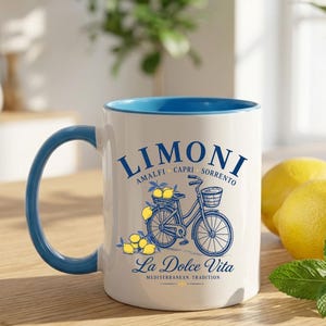May include: A white ceramic mug with a blue interior and handle, featuring a blue graphic of a bicycle with baskets of yellow lemons. The text reads LIMONI AMALFI CAPRI SORRENTO and La Dolce Vita MEDITERRANEAN TRADITION in blue lettering.
