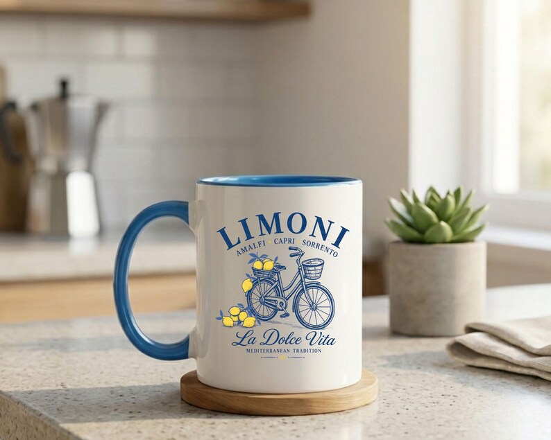 May include: A white ceramic mug with a blue handle and interior rim. The front features a blue graphic of a bicycle with a basket of yellow lemons, accompanied by the text LIMONI, AMALFI CAPRI SORRENTO, La Dolce Vita, and MEDITERRANEAN TRADITION.