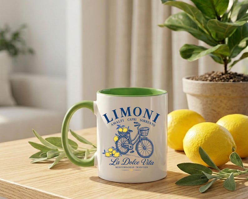 May include: A white ceramic mug with a green interior and handle, featuring a blue graphic of a bicycle with a basket of lemons. The text reads LIMONI AMALFI CAPRI SORRENTO and La Dolce Vita MEDITERRANEAN TRADITION in blue lettering on the front.