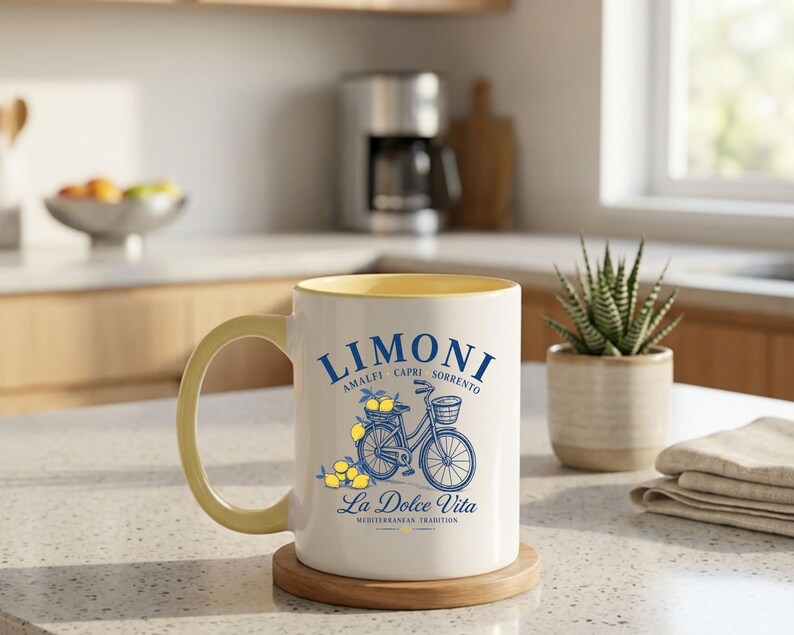 May include: A white ceramic mug with a yellow interior and handle, featuring a blue graphic of a bicycle carrying lemons in a basket. The text reads LIMONI AMALFI CAPRI SORRENTO and La Dolce Vita MEDITERRANEAN TRADITION in blue and yellow lettering.