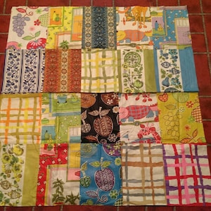 May include: A patchwork quilt made of various fabrics with different patterns and colors, including yellow, green, red, blue, and white. The quilt is made up of 16 squares, each with a different design.