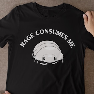 Puede incluir: Una camiseta negra de manga corta con un gráfico de una cochinilla de color gris claro centrado en el pecho. Sobre la cochinilla, el texto RAGE CONSUMES ME está impreso en blanco, en arco y con una fuente sans-serif. El diseño es sencillo.