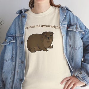 t-shirt with a cute hand-drawn hyrax illustration and the phrase ‘it’s gonna be awawaright’ — funny wholesome animal meme graphic tee.