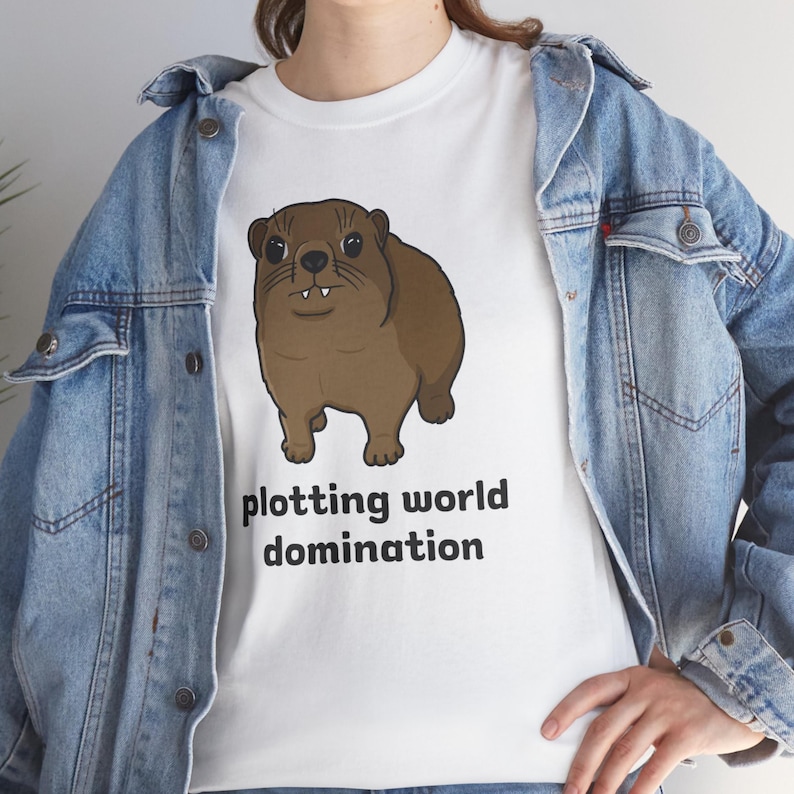 Cute brown hyrax illustration wearing a serious expression with the text “plotting world domination” printed on a t-shirt, funny animal meme graphic tee