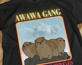 Könnte beinhalten: Schwarzes T-Shirt mit einer gelben und roten Grafik von drei braunen Klippschliefer auf einem Felsen mit blauem Himmel und weißen Wolken im Hintergrund. Die Grafik lautet "AWAWA GANG - THE HYRAXES".