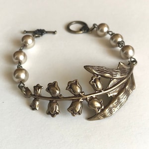 Pulsera vintage de lirio del valle: brazalete floral de latón con perlas beige y cierre de palanca.