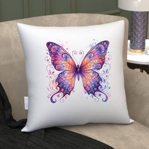 Puede incluir: Coj&iacute;n cuadrado blanco con un dise&ntilde;o de mariposa acuarela colorida. La mariposa tiene alas moradas, naranjas y azules con detalles florales y remolinos. El coj&iacute;n est&aacute; sobre un sof&aacute; de tonos neutros.