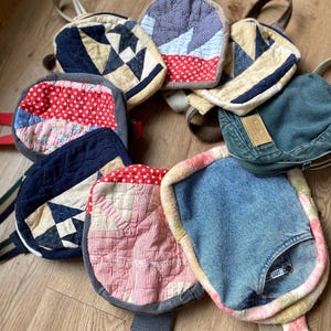 May include: A collection of nine small, handmade bags in various colors and patterns. The bags are made from denim, patchwork fabric, and quilted fabric. Some of the bags have straps and others have handles.