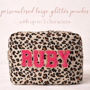 May include: A leopard print glitter pouch with the name "RUBY" in pink, textured letters. The text "personalised large glitter pouches with up to 5 characters" is above the pouch. The pouch is rectangular in shape.