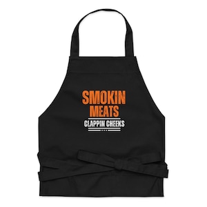 May include: Black apron with the text "Smokin Meats Clappin Cheeks" in orange.