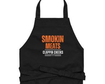 May include: Black apron with the text "Smokin Meats Clappin Cheeks" in orange.