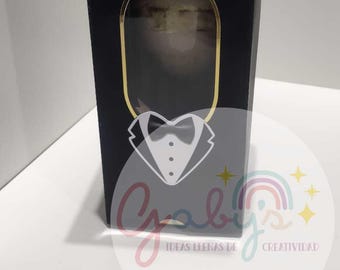 Pode incluir: Caixa de presente preta com alça dourada e janela oval com borda dourada. Um gráfico de smoking está na frente. A caixa tem o texto "Gaby's Ideas Llenas de Creatividad" e um logotipo de arco-íris.