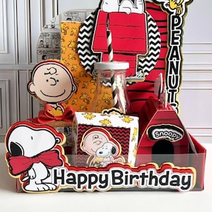 May include: A colorful Snoopy-themed birthday decoration set. It includes Snoopy, Charlie Brown, and Woodstock cutouts, a red doghouse, and a "Happy Birthday" banner. The set features red, yellow, black, and white colors.