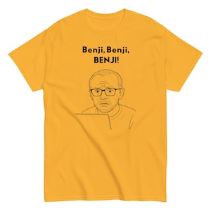 May include: Mustard yellow t-shirt featuring a black and white line drawing of a man wearing glasses and looking concerned. Above the illustration is the text "Benji, Benji, BENJI!"