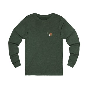 Könnte beinhalten: Dunkelgrünes Langarmshirt mit einem kleinen gestickten Design auf der oberen linken Brust. Das Design zeigt einen Kreis, eine braune Form und eine weiße Form. Das Shirt ist aus einem weichen, bequemen Material.