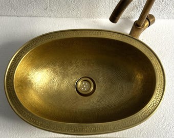 May include: A hammered brass oval sink with a drain in the center. The sink has a decorative border around the edge.