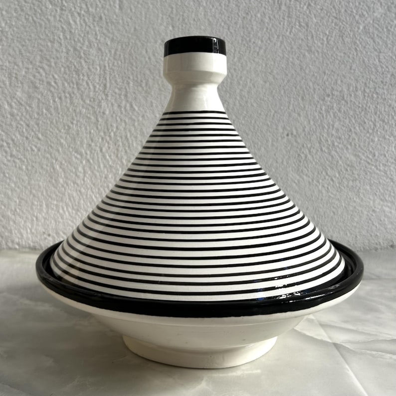 K&ouml;nnte beinhalten: Wei&szlig;e Keramik-Tagine mit einem schwarz-wei&szlig;en Streifenmuster und einem schwarzen Rand.