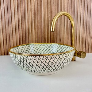 A white ceramic bathroom sink with a green and black geometric pattern and a gold rim. The sink is paired with a gold faucet.