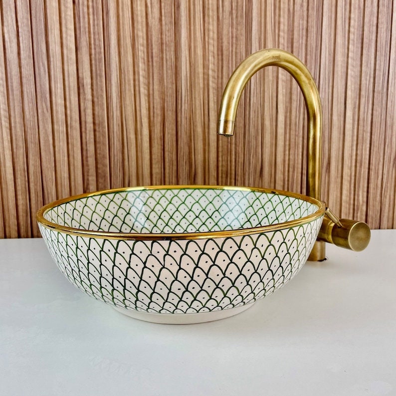 A white ceramic bathroom sink with a green and black geometric pattern and a gold rim. The sink is paired with a gold faucet.