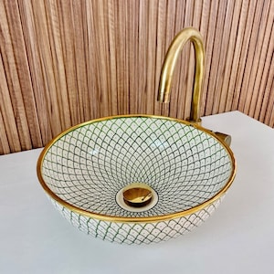 A white ceramic sink with a green and black geometric pattern and a gold rim. The sink has a gold drain cover and is paired with a gold faucet.