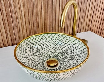 May include: A white ceramic sink with a green and black geometric pattern and a gold rim. The sink has a gold drain cover and is paired with a gold faucet.