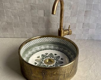 May include: A round, decorative bathroom sink with a gold-colored exterior and a patterned interior. The interior features a white background with a green and black floral design. A gold faucet is mounted above the sink.