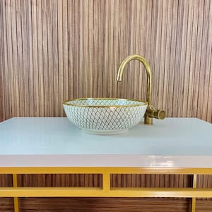 A white ceramic sink with a gold rim and a black and white geometric pattern. The sink is on a light blue countertop with a yellow frame.