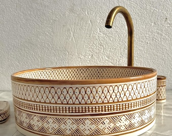 May include: A white ceramic bathroom sink with a brown geometric pattern around the rim. The sink is round and has a brass faucet.
