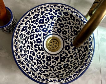 Puede incluir: Un lavabo de cerámica blanca con un patrón floral azul y blanco. El lavabo tiene un desagüe de latón y está diseñado para un baño.