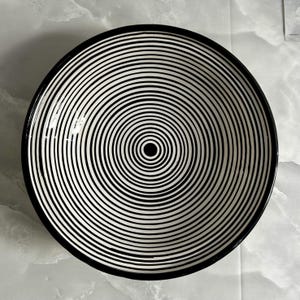 K&ouml;nnte beinhalten: Eine gro&szlig;e, wei&szlig;e Keramiksch&uuml;ssel mit einem schwarzen und wei&szlig;en konzentrischen Kreisdesign. Die Sch&uuml;ssel hat einen schwarzen Rand.