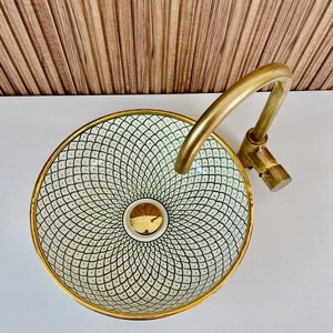 A white ceramic sink with a gold rim and a green and white geometric pattern. The sink is paired with a gold faucet.