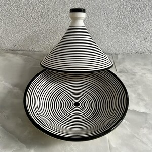 K&ouml;nnte beinhalten: Eine schwarze und wei&szlig;e Keramik-Servierplatte mit Deckel. Die Platte hat ein konzentrisches Kreis-Muster und der Deckel hat ein gestreiftes Muster.