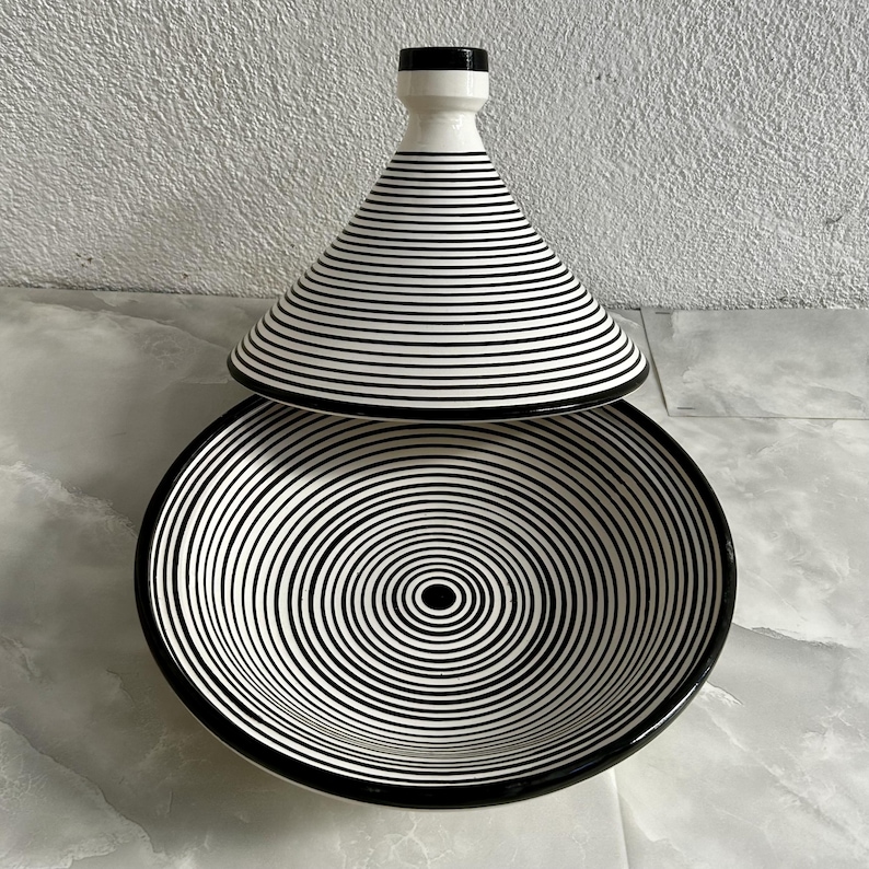 K&ouml;nnte beinhalten: Eine schwarze und wei&szlig;e Keramik-Servierplatte mit Deckel. Die Platte hat ein konzentrisches Kreis-Muster und der Deckel hat ein gestreiftes Muster.
