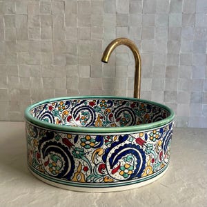 Peut inclure: Un lavabo rond en céramique avec un motif floral coloré bleu, jaune, rouge et vert. L'évier a un bord vert et un robinet en laiton. Le lavabo est un élément décoratif de salle de bain.