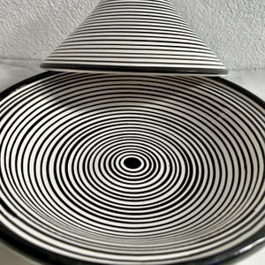 K&ouml;nnte beinhalten: Eine schwarze und wei&szlig;e Keramik-Tagine mit einem konzentrischen Kreis-Muster. Die Tagine hat einen Deckel mit einem &auml;hnlichen Muster.