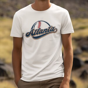 May include: White t-shirt featuring a baseball graphic and the word "Atlanta" in a vintage-style font.