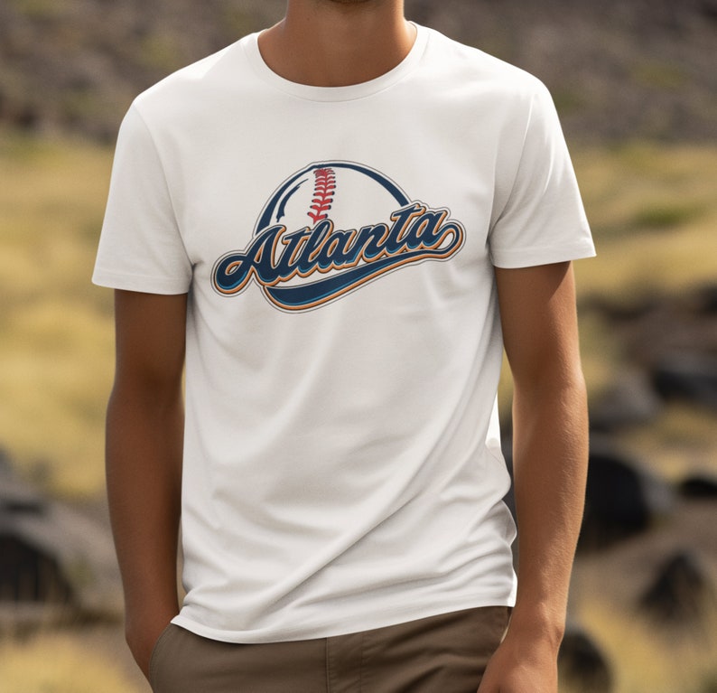 May include: White t-shirt featuring a baseball graphic and the word "Atlanta" in a vintage-style font.