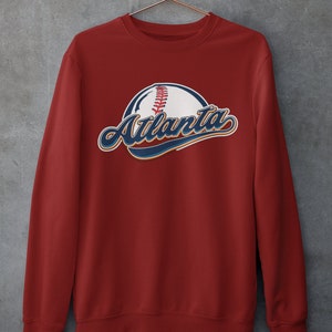 May include: Red sweatshirt featuring a baseball and the word "Atlanta" in blue and white lettering.