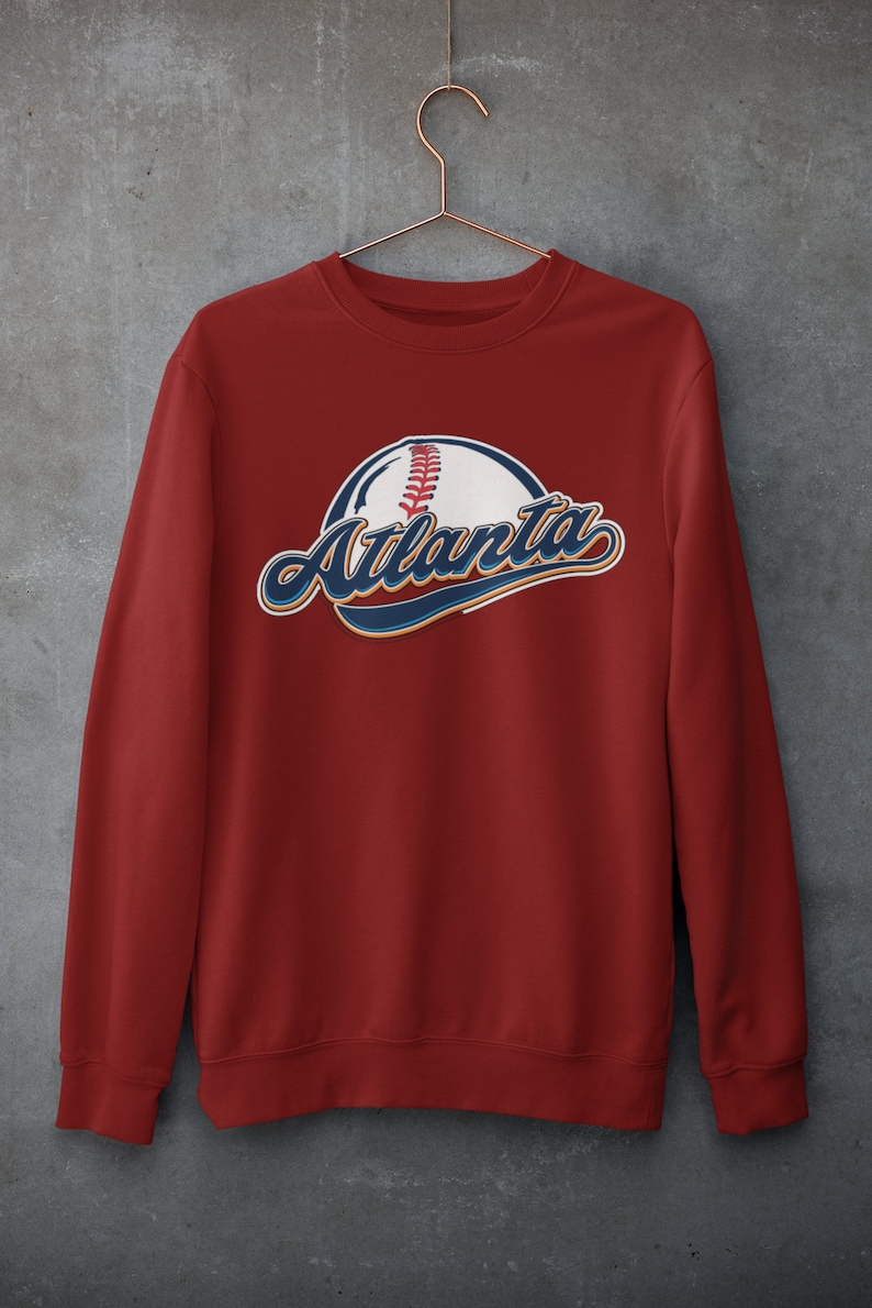 May include: Red sweatshirt featuring a baseball and the word "Atlanta" in blue and white lettering.