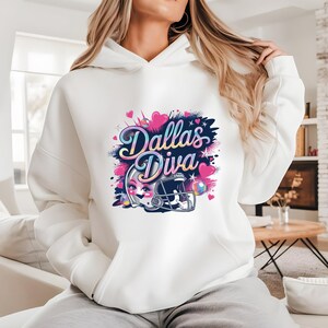 May include: White hoodie with a colorful graphic that says "Dallas Diva." The design includes a football helmet, hearts, and a cartoon face. The hoodie is a casual, comfortable style.