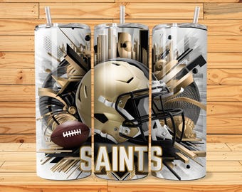 May include: A white tumbler with a gold and black design featuring a football helmet, football, and the word "SAINTS". The design includes geometric shapes and a cityscape.