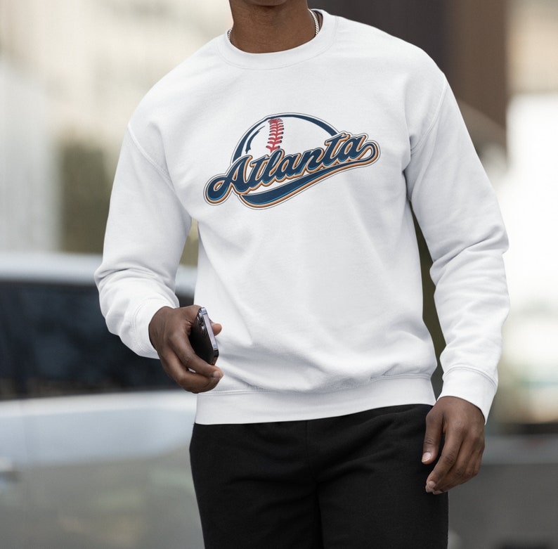 May include: White long-sleeved sweatshirt with a navy blue and orange graphic of a baseball with the word "Atlanta" in a stylised font.