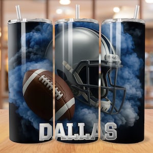 May include: A stainless steel tumbler featuring a football, helmet, and blue smoke design. The word "DALLAS" is displayed in silver block letters. The tumbler has a black lid and a clear straw.