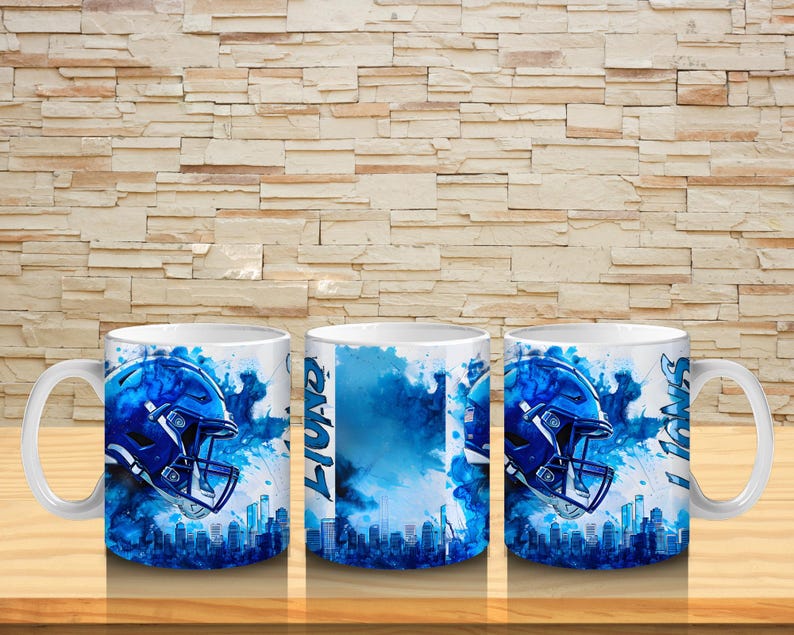 Puede incluir: Taza de cer&aacute;mica blanca con un dise&ntilde;o de casco de f&uacute;tbol americano azul y una silueta de ciudad. La taza presenta la palabra "Lions" y detalles en acuarela azul. La taza est&aacute; sobre una superficie de madera.