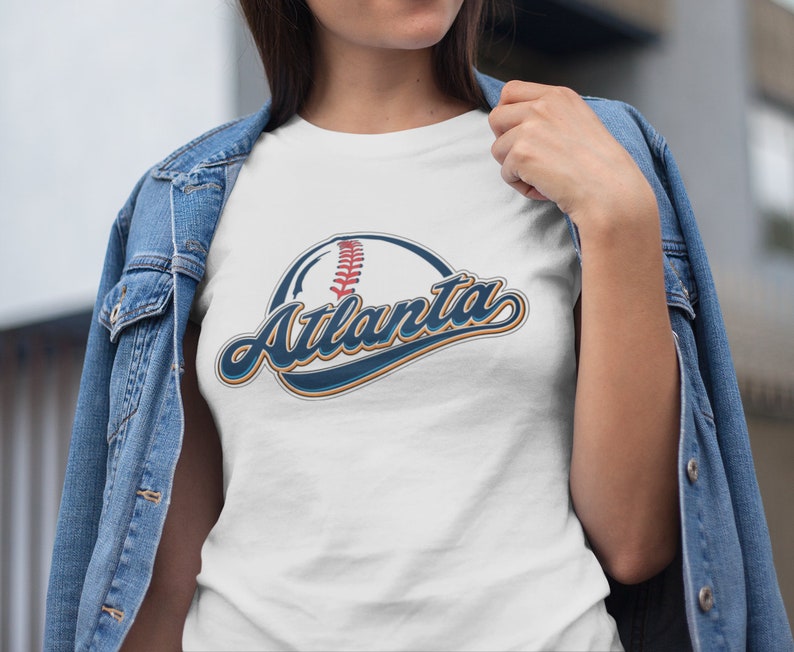 May include: White t-shirt featuring a blue and orange baseball graphic with the text "Atlanta" in a vintage style font.