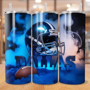 May include: Three stainless steel tumblers with a Dallas Cowboys theme. Each tumbler features a blue football helmet, a brown football, and the word "DALLAS" in blue. The design is set against a backdrop of blue smoke.