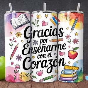 Pu&ograve; includere: Tre bicchieri in acciaio inox bianchi con disegni ad acquerello rosa, giallo e blu. I bicchieri presentano una variet&agrave; di illustrazioni a tema scolastico, tra cui libri, matite, righelli e mele. Il testo "Gracias por ense&ntilde;arme con el coraz&oacute;n" &egrave; stampato in nero sui bicchieri.