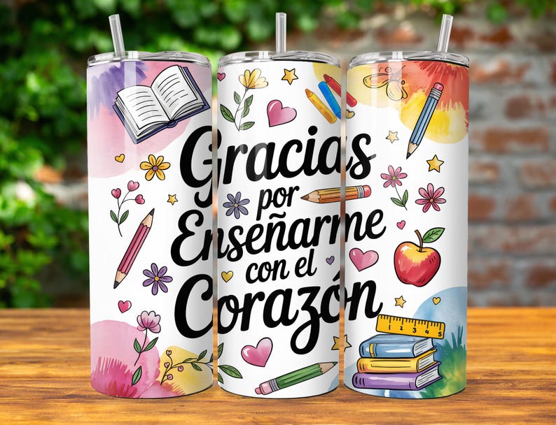 Pu&ograve; includere: Un bicchiere bianco con un design colorato che presenta un libro, matite, cuori, stelle e un righello. Il testo sul bicchiere recita "Gracias por ense&ntilde;arme con el coraz&oacute;n".